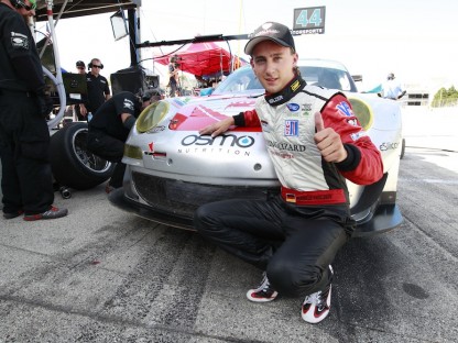 Marco Holzer kneeling near Porsche after taking at Road America ALMS