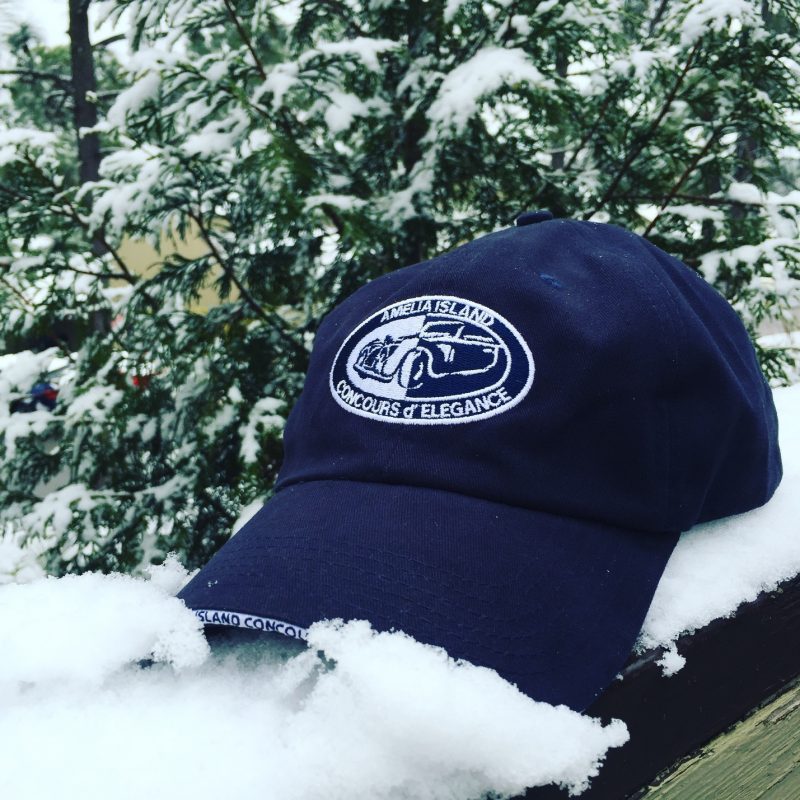 an Amelia Island Concours D'Elegance baseball cap resting on a porch railing covered in snow