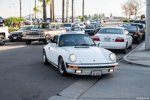 White 1989 Carrera 3.2 pulls into Radwood 2 as the passenger waves to the camera