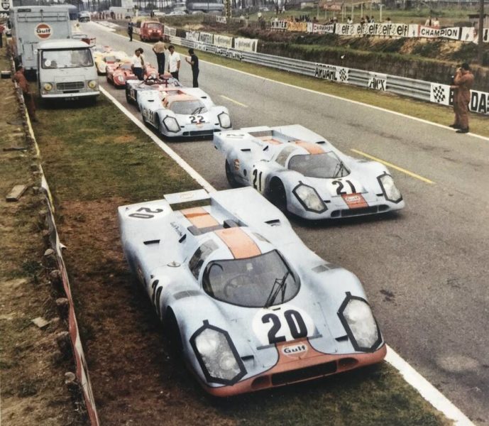 Three Porsche 917KH in Gulf Oil livery on a road, being used for filming Le Mans